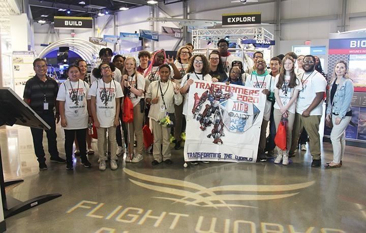  A group of students and workshop facilitators smile to the camera with a banner. 